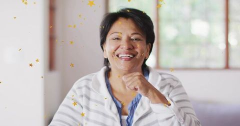 Smiling senior woman relaxing on sofa with gold star confetti in sunlit home