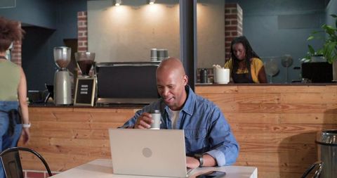 African American man working on laptop and enjoying coffee in cozy rustic cafe