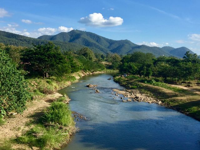 River flowing through lush, green landscape with distant mountains under a clear, blue sky. Ideal for nature, travel and eco-tourism promotions or calming scenery backgrounds.