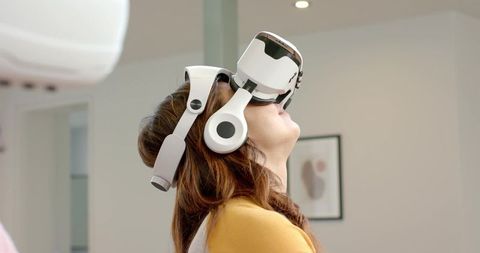 Mid adult woman experiencing virtual reality with white VR headset and headphones in modern room