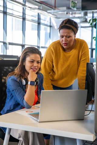 Diverse female coworkers collaborating and reviewing chart on laptop in modern open office