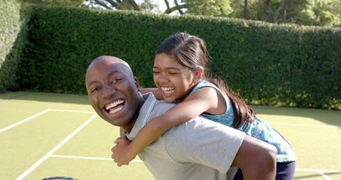 Father Giving Daughter Piggyback Ride on Tennis Court