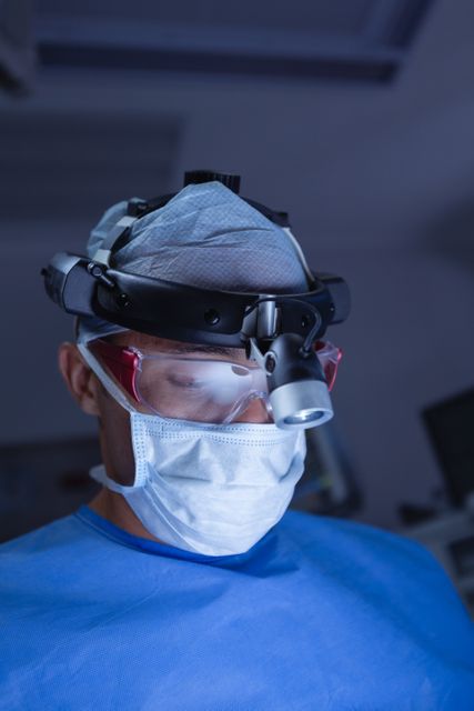 Surgeon wearing surgical headlight and protective gear performing an operation in a hospital operating room. Ideal for use in medical articles, healthcare websites, educational materials, and promotional content for medical equipment.