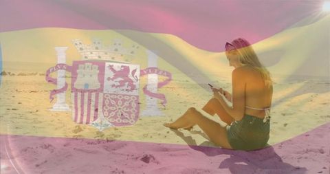 Woman on sandy shore with spanish flag overlay relaxing with smartphone