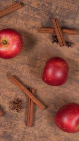 Vertical video panning over rustic wood table with red apples, cinnamon sticks, star anise