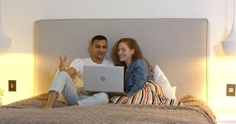 Couple Relaxing on Bed with Laptop, Celebrating Engagement