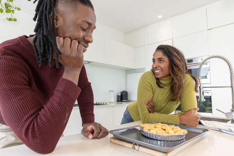 Interracial couple baking pie in modern white kitchen leaning on counter smiling admiring pie