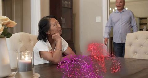 Senior asian couple sharing playful augmented reality particles at cozy dining table