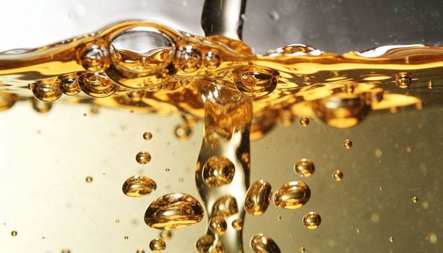 Golden liquid pouring with rising bubbles and reflective droplets macro closeup