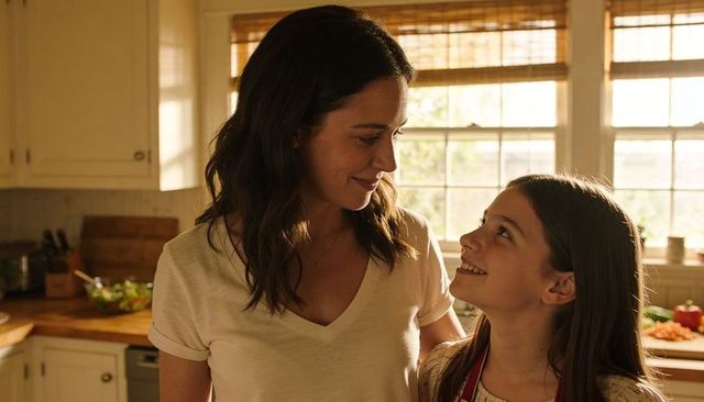 Mother and daughter preparing fresh salad in sunlit kitchen sharing warm smile