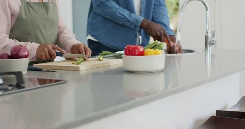 Mature couple preparing green onions on modern bright kitchen island with fresh peppers