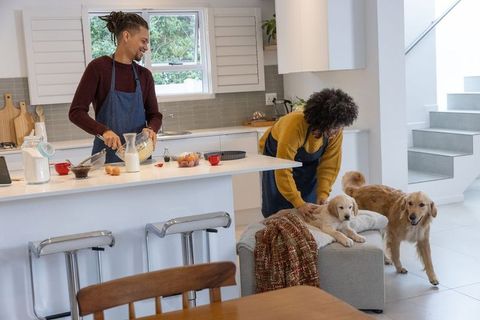 African american couple mixing batter while petting golden retrievers in modern kitchen