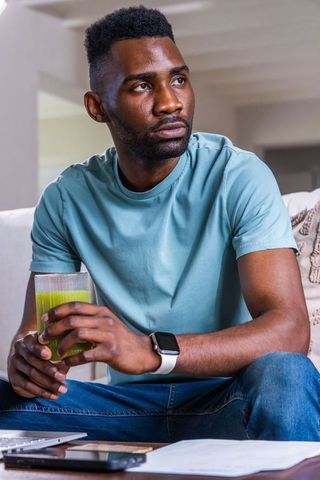 African man sipping green juice on sofa wearing smartwatch, casual wellness lifestyle