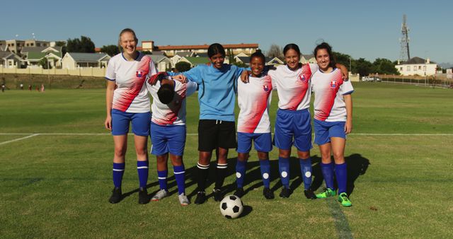 Team of diverse female football players standing with ball and embracing on sunny sports field. Active lifestyle, sport, competition, hobby and wellbeing, unaltered.