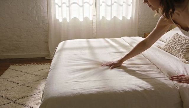 Smoothing linen duvet on minimalist boho bed with sunlit curtains and macrame pillow