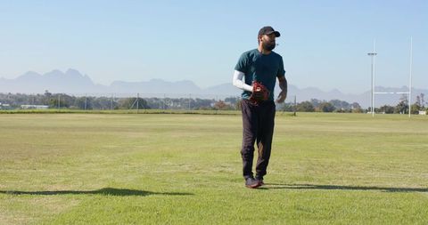 Baseball player standing on grassy field holding glove wearing cap with mountain skyline