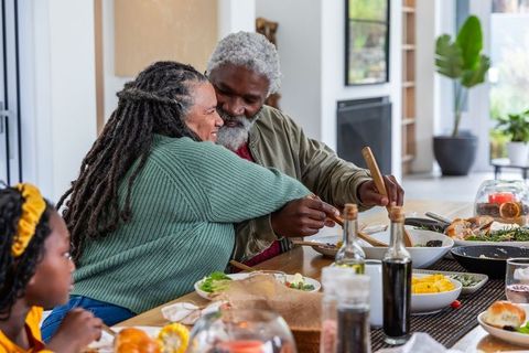 Senior african american couple hugging and serving roast at cozy family dinner