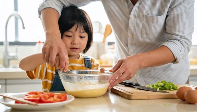 Parent guiding child whisking batter in bright kitchen capturing family cooking moment