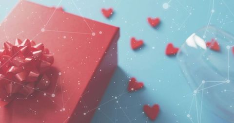 Red gift box with bow on blue background, scattered heart confetti and soft dotted overlay