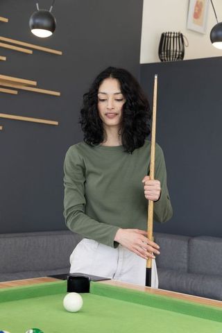 Woman holding cue stick beside pocket on green pool table in modern lounge interior
