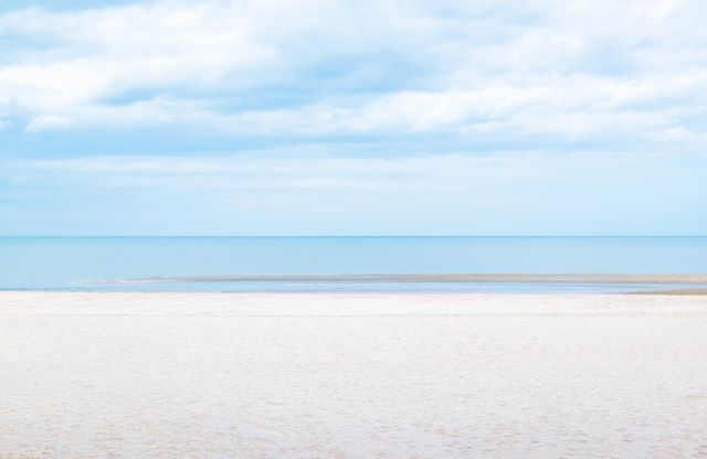 Image showcases a tranquil sandy beach meeting a calm ocean under a blue sky with clouds. Ideal for travel brochures, meditation and relaxation products, coastal property advertisements, and summer destination promotions.