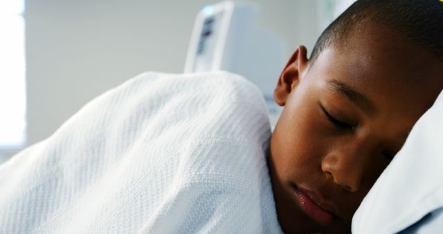 Young boy resting peacefully in a hospital bed, wrapped in a white blanket. This image can be used for healthcare advertisements, children's medical care brochures, articles about pediatric healthcare, and well-being promotions.