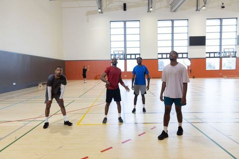 Male teammates watching basketball arc toward hoop on indoor court