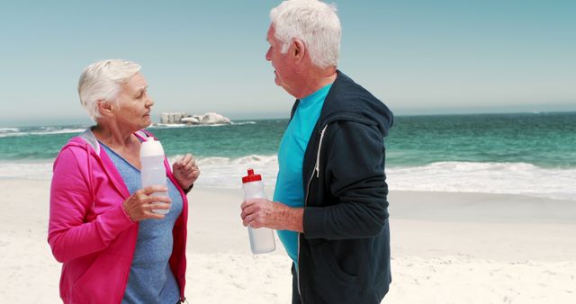 Old retired couple drinking water after sport on the beach