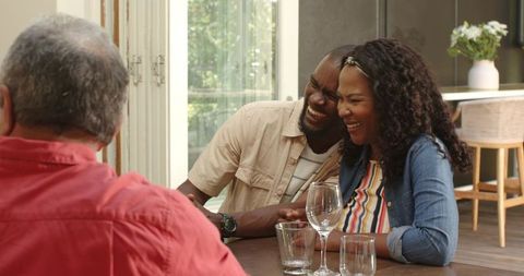 Sunlit family laughing around wooden dining table sharing wine, stories and warm conversation