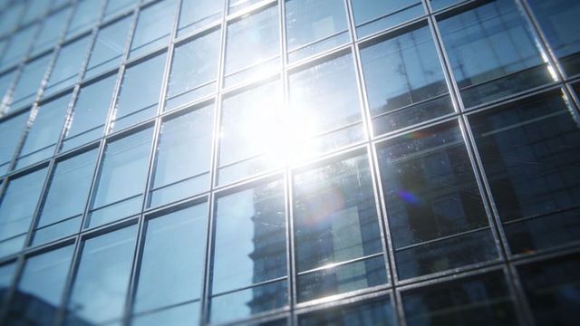 Sunlit glass facade with strong reflections and grid pattern on modern high-rise