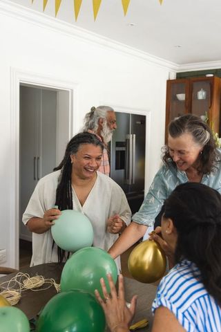 Multigenerational friends decorating kitchen with green and gold balloons, joyful gathering