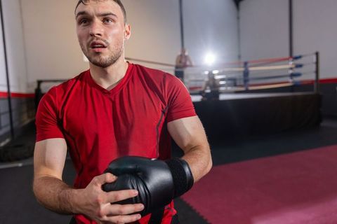 Boxer catching breath after intense round wearing red shirt and black gloves in gym
