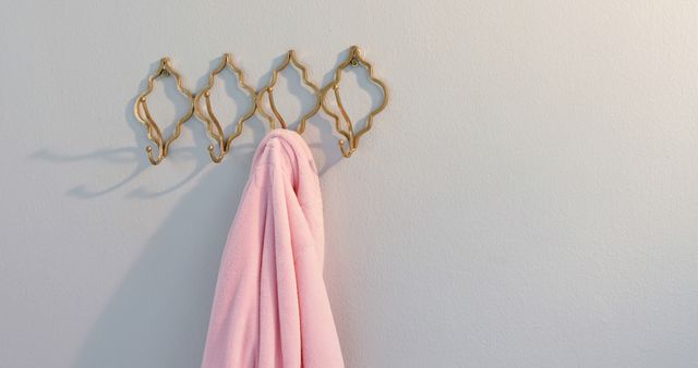 Vintage-style hooks on neutral wall with pink robe hanging, suitable for content about interior design, bathroom organization, minimalist decor or simple living.