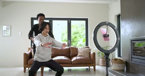 African american female trainer guiding man doing squat during at-home fitness video