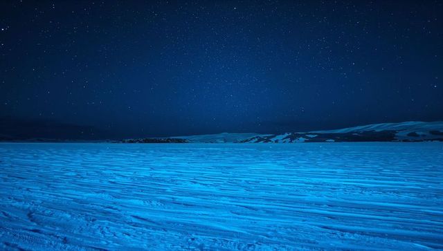 Arctic snow plain under starry night with wind-swept ridges and blue airglow