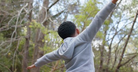 African american boy standing arms outstretched in forest wearing light gray hoodie