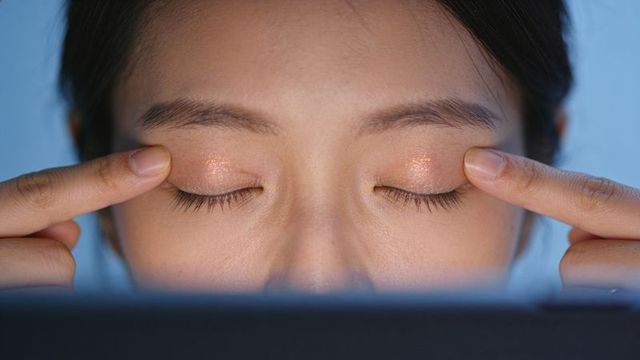 Glitter eyeshadow application closeup with fingers pressing eyelids and blue monitor glow
