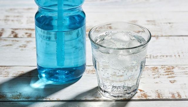 Sparkling water with ice and blue bottle casting shadow on sunlit rustic weathered wood