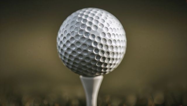 Macro closeup of golf ball resting on tee showing dew drops and detailed dimple texture