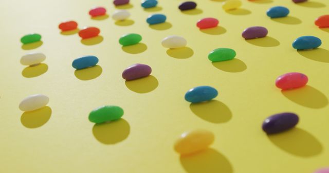 Image of overhead view of rows of multi coloured sweets over yellow background. fusion food and sweets concept.