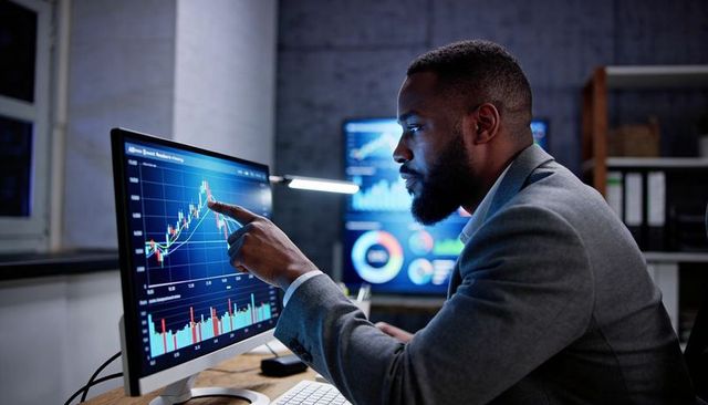 Business analyst pointing at rising stock chart on desktop monitor in modern office