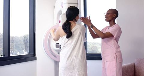 Technologist positioning patient for mammogram at modern breast imaging unit in clinic