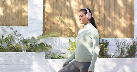 Asian woman balancing on patio in mint top and pink headphones, fitness and wellness