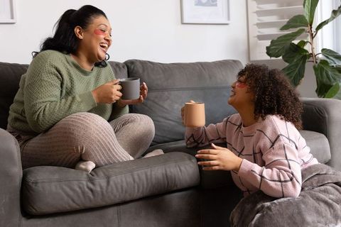 African american women laughing and sipping coffee on cozy gray sofa at home