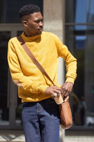 African american man in mustard sweater placing coffee cup into brown crossbody bag