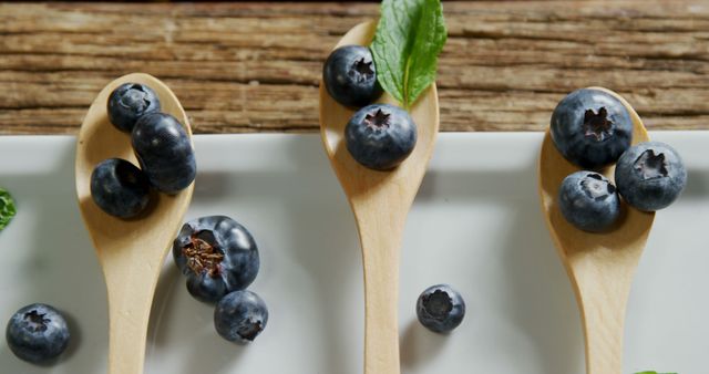 Depicting a closeup of fresh blueberries resting on wooden spoons along with mint leaves, this image can be used for food and nutrition blogs, healthy eating articles, vegan recipes, superfood promotions, or organic product advertisements. The rustic background enhances the natural and fresh appeal of the scene.