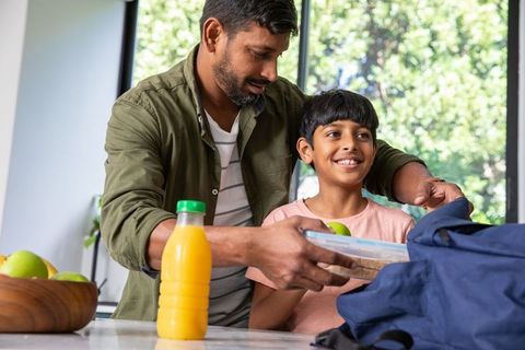 Father packing lunch for son at kitchen counter