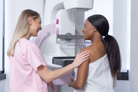 Breast imaging technologist guiding African-American woman during mammogram screening