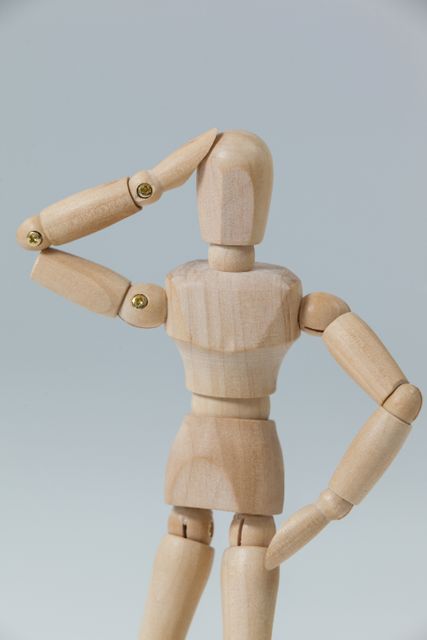 Wooden mannequin standing with hand on head, appearing confused or deep in thought. Useful for illustrating concepts of confusion, decision making, problem solving, and contemplation. Ideal for educational materials, creative projects, and artistic expressions.