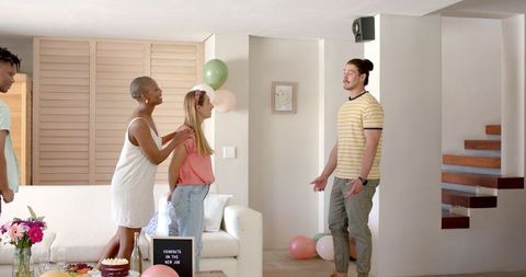 Friends joyfully celebrating new job indoors with balloons and cake